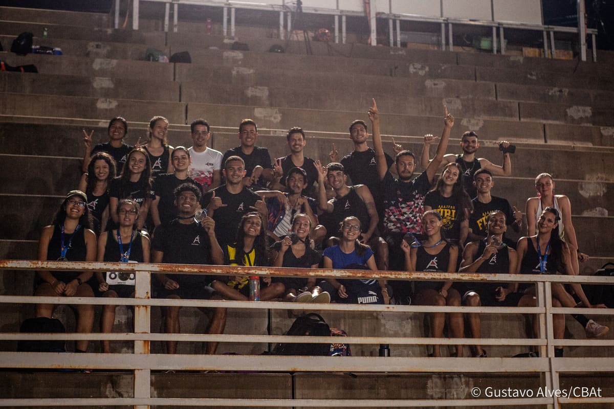 Equipe da Atletismo-UEM reunida na arquibancada à noite, comemorando