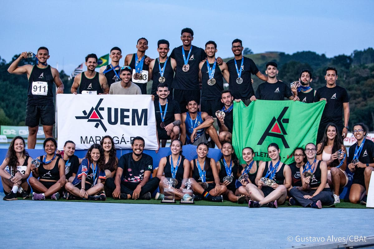 Equipe completa da Atletismo-UEM em foto de grupo com faixa da UEM Maringá e bandeira do time